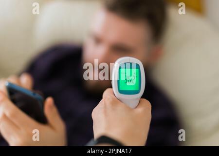 Gros plan du thermomètre frontal numérique infrarouge dans la main, examen de la fièvre et mesures pour prévenir et filtrer les personnes vérifier la température du corps pendant Banque D'Images
