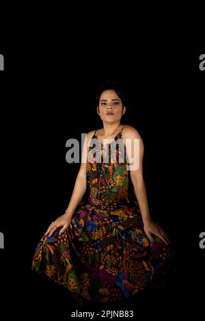 Portrait d'une jeune femme assise sur un tabouret posant pour une photo. Isolé sur fond noir. Banque D'Images