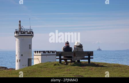 Fife, Écosse, Royaume-Uni. 3 avril 2023. Le soleil et le ciel bleu avec de belles vues panoramiques auraient pu faire croire à tous les visiteurs qu'ils étaient dans le sud de la France au lieu de sur la côte du Fife, bien qu'après des températures négatives pendant la nuit et la température du milieu de la matinée à 8 degrés centigrades et se réchauffant jusqu'à un peu plus de 10 degrés dans l'après-midi peut-être était-il légèrement plus frais que le continent. Sur la photo : un couple assis sur un banc et profiter de la vue à côté du phare d'Elie Ness qui est situé sur le promentary entre Inchkeith et l'île de May. Banque D'Images