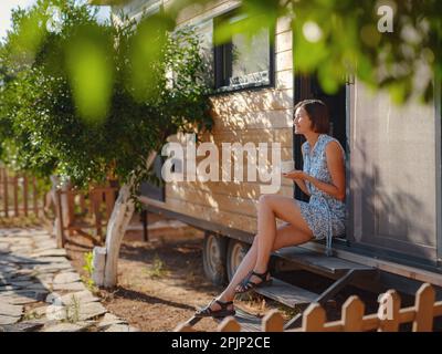 La femme boit du café, la routine du matin près de sa petite maison. Première propriété. Petit appartement dans le jardin d'été. Minimalisme. Entrée en marche. Vivre seul. Banque D'Images