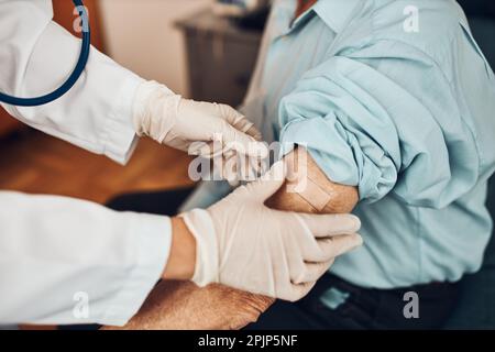 Médecin mettant un plâtre à la place de l'injection du vaccin à un patient d'homme âgé. Vaccin Covid-19 ou coronavirus. Médecin portant un manteau blanc et Banque D'Images