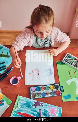 Petite fille de pré-chooler peignant une image en utilisant des peintures colorées et des crayons. Enfant s'amusant à prendre une photo pendant un cours d'art en classe Banque D'Images