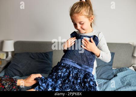 Mère et sa fille ouvrant la boîte avec robe commandée à la maison sur le canapé. Maman client en ligne tenant la robe. Service de livraison mode concept Banque D'Images