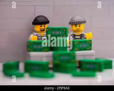 Tambov, Fédération de Russie - 25 mars 2023 deux mini-figurines de voleur de Lego assis derrière un bureau avec une pile d'argent dessus. Banque D'Images