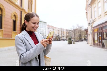 Femme en tenue décontractée marchant dans la ville et messagerie en ligne à l'aide de son téléphone mobile. Banque D'Images