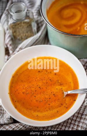 Soupe de poivre et de tomate cuits dans une assiette blanche et une marmite verte, herbes d'origan séchées dans un verre sur une nappe. Banque D'Images