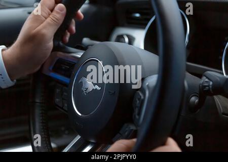 Los Angeles, États-Unis - avril 2017 : un chauffeur de sexe masculin garde les mains sur le volant d'une Ford Mustang, gros plan. Tableau de bord Ford Mustang avec volant. Volant de la planche de bord intérieure de la voiture. Banque D'Images