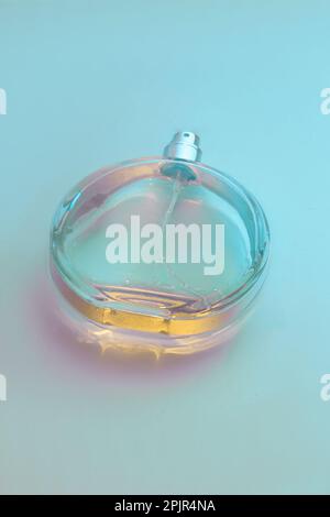 Vue de dessous d'une bouteille de parfum vaporisée sur une table en verre de couleur bleue. Banque D'Images