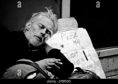 Un homme sans domicile tente de dormir dans une porte et a soutenu un panneau sur un morceau de carton demandant aux passants de l'aide. Banque D'Images