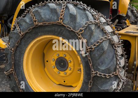 Grand pneu de tracteur en caoutchouc noir avec chaînes en acier. Banque D'Images