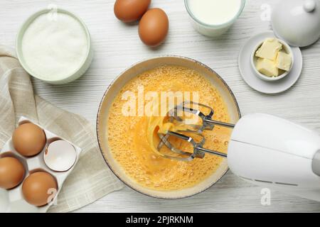 Battre les œufs dans un bol avec un batteur sur une table en bois blanc, ponter à plat Banque D'Images