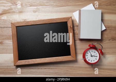 Tableau noir vierge avec carnets et réveil sur table en bois, posé à plat. Espace pour le texte Banque D'Images