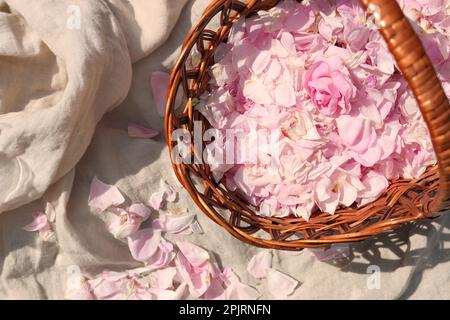 Panier en osier de beaux pétales de rose sur tissu beige, plat Banque D'Images