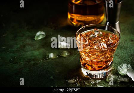 Cocktail Godfather avec whisky scotch, liqueur d'amaretto et glace. Fond de comptoir de bar sombre, outils de bar, espace de copie Banque D'Images