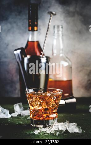Cocktail Godfather avec whisky scotch, liqueur d'amaretto et glace. Fond de comptoir de bar sombre, outils de bar, espace de copie Banque D'Images