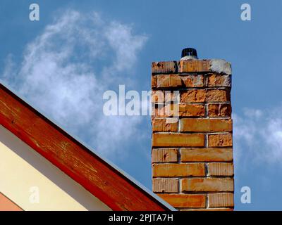 Cheminée isolée en brique d'argile qui se détériore avec une surface abîmée et écalée. garniture en bois sur le mur d'extrémité du toit de la maison. élévation extérieure en stuc blanc. Banque D'Images