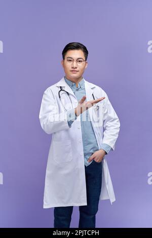 Jeune beau docteur homme portant le stéthoscope, souriant gai présenter et pointer avec la paume de la main Banque D'Images