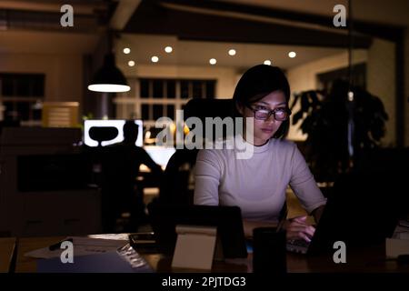 Femme d'affaires asiatique portant des lunettes, assise au bureau, utilisant un ordinateur portable qui travaille tard au bureau Banque D'Images