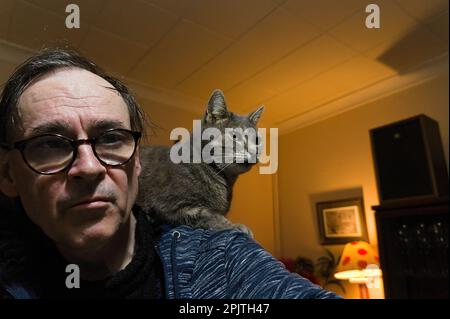 Un homme portant des lunettes avec un chat tabby assis sur son épaule à la maison Banque D'Images