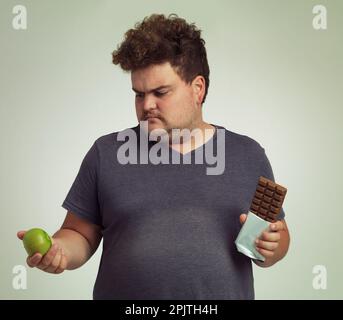 Désolé M. Apple - vous perdez ce tour. un homme en surpoids décidant entre une pomme et une barre de chocolat. Banque D'Images