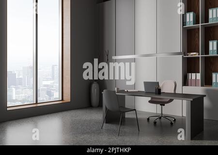 Intérieur de bureau d'affaires moderne et sombre avec ordinateur portable sur le bureau, vue latérale sur le sol en béton gris. Coin PDG avec étagère, fauteuil et fenêtre panoramique Banque D'Images