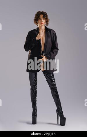 Polédanseuse en veste et bottes en cuir posé en studio sur fond gris Banque D'Images