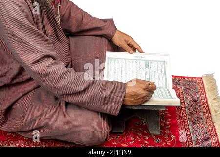 Homme musulman assis et lisant le Coran sur le tapis de prière isolé sur fond blanc Banque D'Images