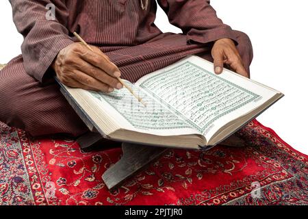 Homme musulman assis et lisant le Coran sur le tapis de prière isolé sur fond blanc Banque D'Images