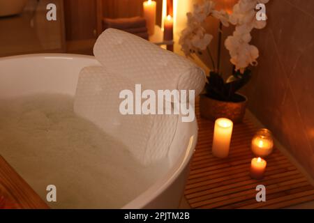 Baignoire avec eau mousseuse et oreiller de bain doux entouré de bougies à l'intérieur Banque D'Images