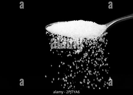 Macro photographie d'une cuillère à café avec le sucre blanc en fricleur sur un fond noir, espace de copie. Banque D'Images