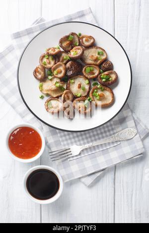 Champignons shiitake frits faits maison avec oignons verts en gros plan sur une assiette blanche. Vue verticale du dessus Banque D'Images