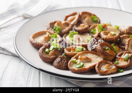 Hors-d'œuvre champignons shiitake frits avec oignons verts en gros plan sur une assiette blanche sur la table. Horizontale Banque D'Images