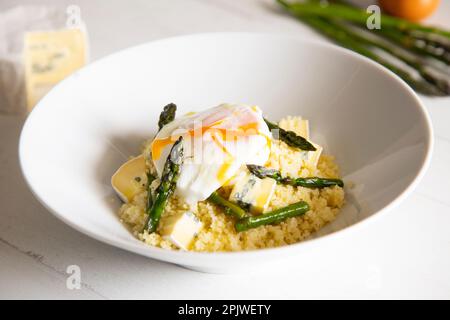 Plat au couscous avec un œuf frit, des asperges vertes et du fromage bleu. Banque D'Images