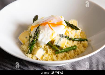 Plat au couscous avec un œuf frit, des asperges vertes et du fromage bleu. Banque D'Images