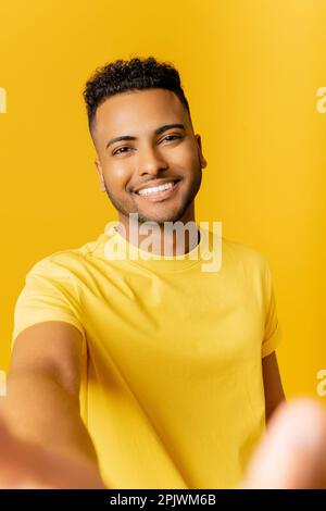 Gentil Indien attrayant prenant le selfie, portant décontracté t-shirt sourire joyeusement regarder l'appareil photo debout isolé sur fond jaune, pov arabe homme faisant appel vidéo, enregistrement vidéo Banque D'Images