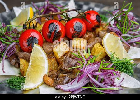 Gros plan de la viande lentement cuite avec des champignons et des pommes de terre, des tomates grillées, des herbes et du citron Banque D'Images