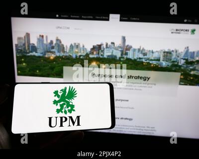 Personne tenant un téléphone portable portant le logo de la société forestière finlandaise UPM-Kymmene Oyj à l'écran, devant la page Web des entreprises. Mise au point sur l'affichage du téléphone. Banque D'Images