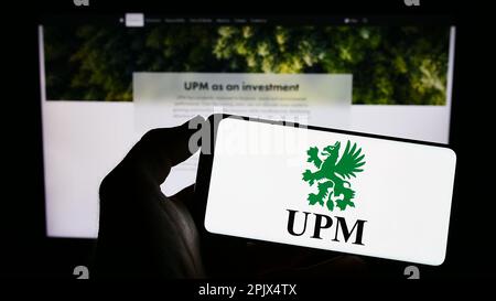 Personne tenant un téléphone portable portant le logo de la société forestière finlandaise UPM-Kymmene Oyj à l'écran devant la page Web des entreprises. Mise au point sur l'affichage du téléphone. Banque D'Images