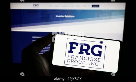 Personne détenant un smartphone portant le logo de la société américaine franchise Group Inc (FRG) à l'écran en face du site Web. Mise au point sur l'affichage du téléphone. Banque D'Images