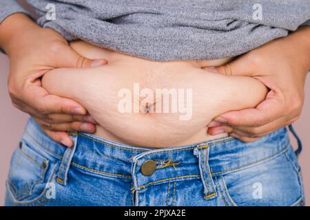 FAT main de femme tenant trop de graisse du ventre isolé sur fond rose. Surpoids ventre gras de la femme. Concept de régime alimentaire et de soins de santé du corps des femmes Banque D'Images