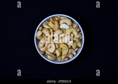 Noix de cajou dans une tasse en céramique blanche. Noix de cajou sur fond noir. Banque D'Images