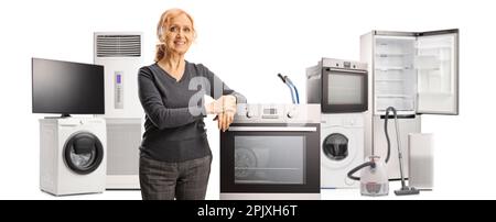 Femme mûre souriante penchée sur un four et d'autres accessoires à la maison dans le dos isolé sur fond blanc Banque D'Images