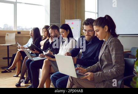 Groupe de personnes lisant ou utilisant des ordinateurs portables en attendant une présentation professionnelle au bureau Banque D'Images