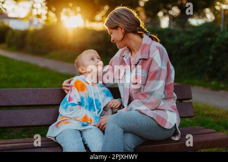 mère et fils s'assoient sur un banc de parc aux rayons du soleil couchant. le concept d'une famille. Fête des mères. belle fille (mère) avec un garçon (fils) Banque D'Images