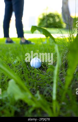 Balle de golf située sur l'herbe rugueuse et golfeur à la recherche de la balle de golf dans les arbres en une journée ensoleillée en Suisse. Banque D'Images