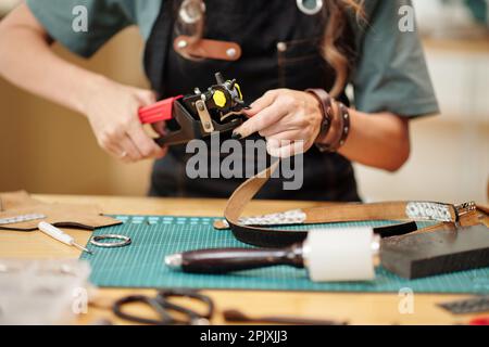 Mains d'une femme utilisant une perforatrice rotative en cuir lors d'une intervention sur la ceinture pour le client Banque D'Images