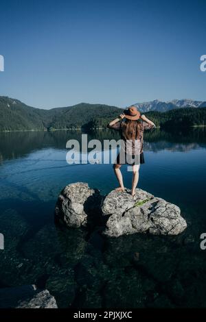 Une jeune femme se tient sur une côte rocheuse, contemplant la vue sur les montagnes majestueuses et la mer au loin Banque D'Images