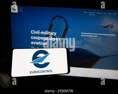 Personne tenant un téléphone portable avec logo de l'organisation de gestion du trafic aérien Eurocontrol sur écran en face de la page web. Mise au point sur l'affichage du téléphone. Banque D'Images
