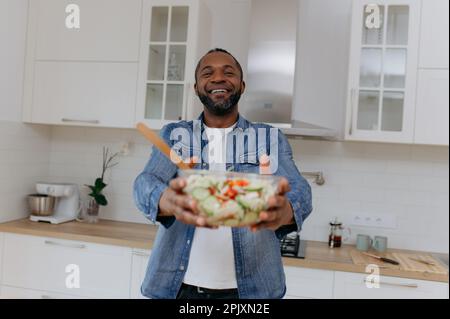 Un homme afro-américain tient une salade dans la cuisine. Banque D'Images