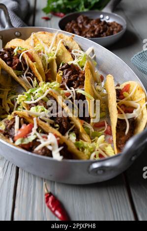 Tacos avec bœuf mexicain cuit lentement, fromage, tomates et laitue sur fond rustique de table Banque D'Images